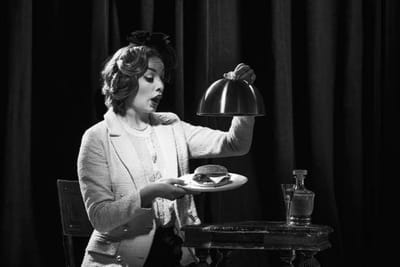 A woman lifting a silver cloche from a plate