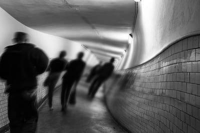 Figures walking away through a curved tiled tunnel, blurred by movement