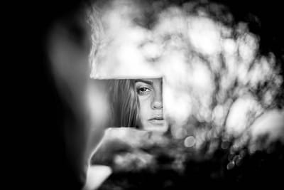 A face half-hidden behind branches, caught in a fragment of mirror